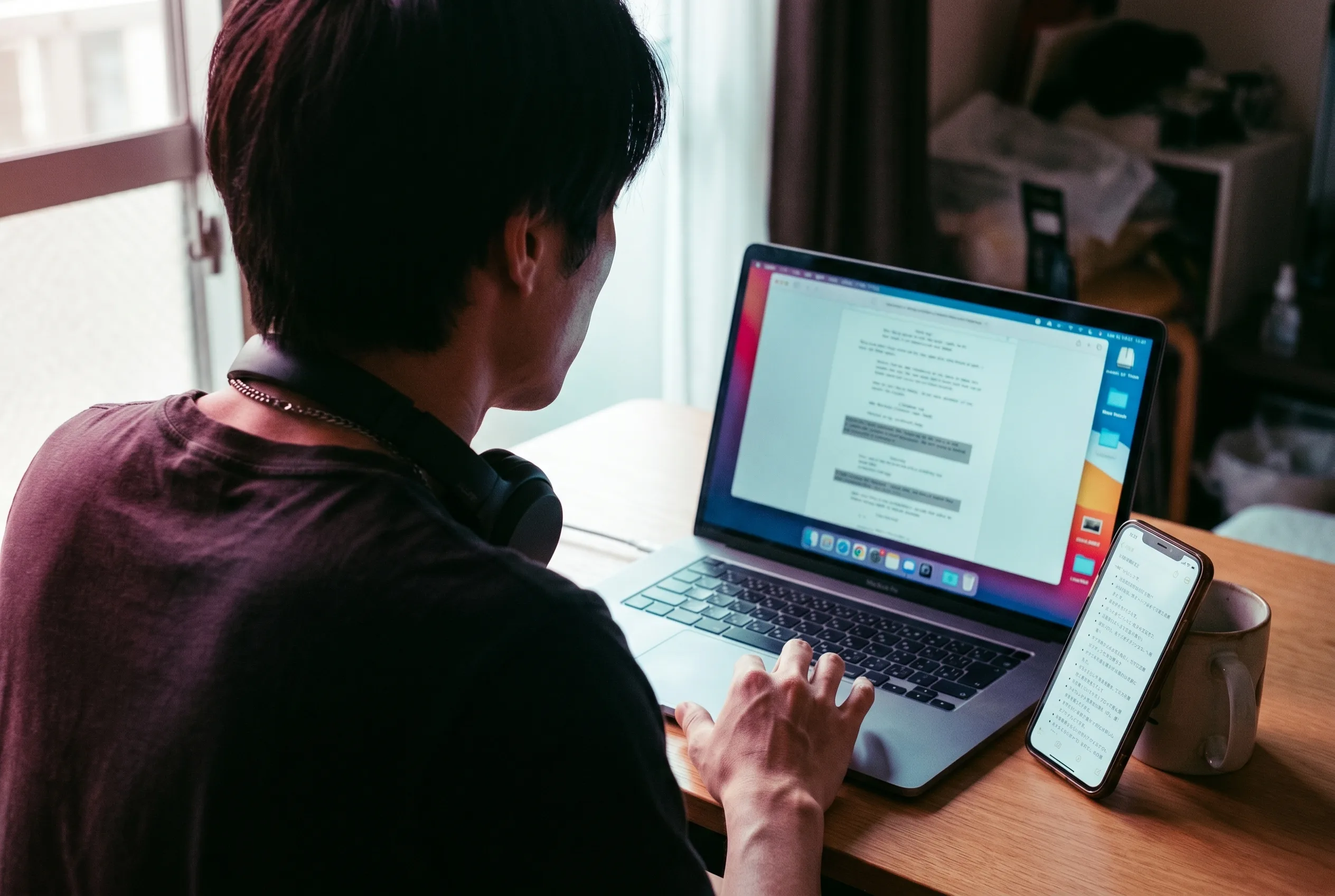 Over-the-shoulder view of a creator's laptop screen showing a timestamped UGC ad script, with a phone beside it displaying a list of hook lines, rendered by the Playcut Actor Engine