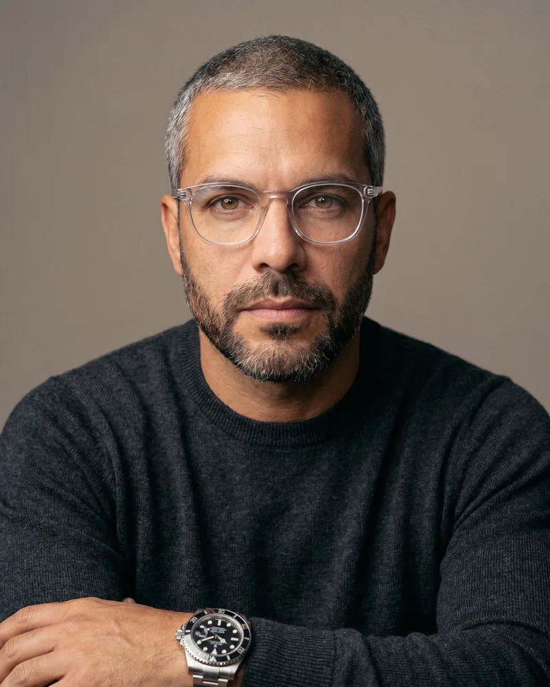 Custom AI avatar Andre Laurent — a mid-40s spokesperson with clear-frame glasses and a steel dive watch — in a clean studio headshot, the same avatar reused across every surface, rendered by the Playcut Actor Engine