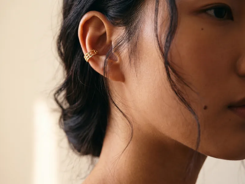 Macro beauty editorial detail of the same custom AI actor Mira Chen's left ear with her signature gold ear cuff in tack-sharp detail, warm window light, Playcut Macro Detail filter