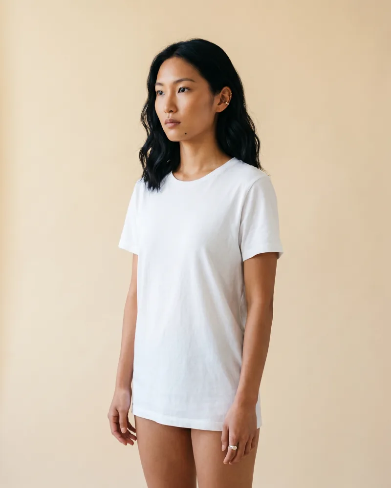 Editorial studio portrait of the same custom AI actor Mira Chen standing against a seamless warm cream paper backdrop in a clean white crewneck tee, soft top-diffused daylight, base reference for product compositing, Playcut Actor Engine generation