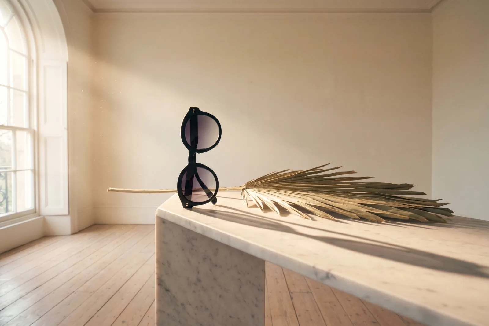 Theatrical editorial product photograph of unbranded oval-frame matte black acetate sunglasses with smoky-grey gradient lenses on a Carrara marble plinth in an empty cream gallery room, dried palm leaf casting a long dramatic afternoon shadow, painterly staging, Playcut generation