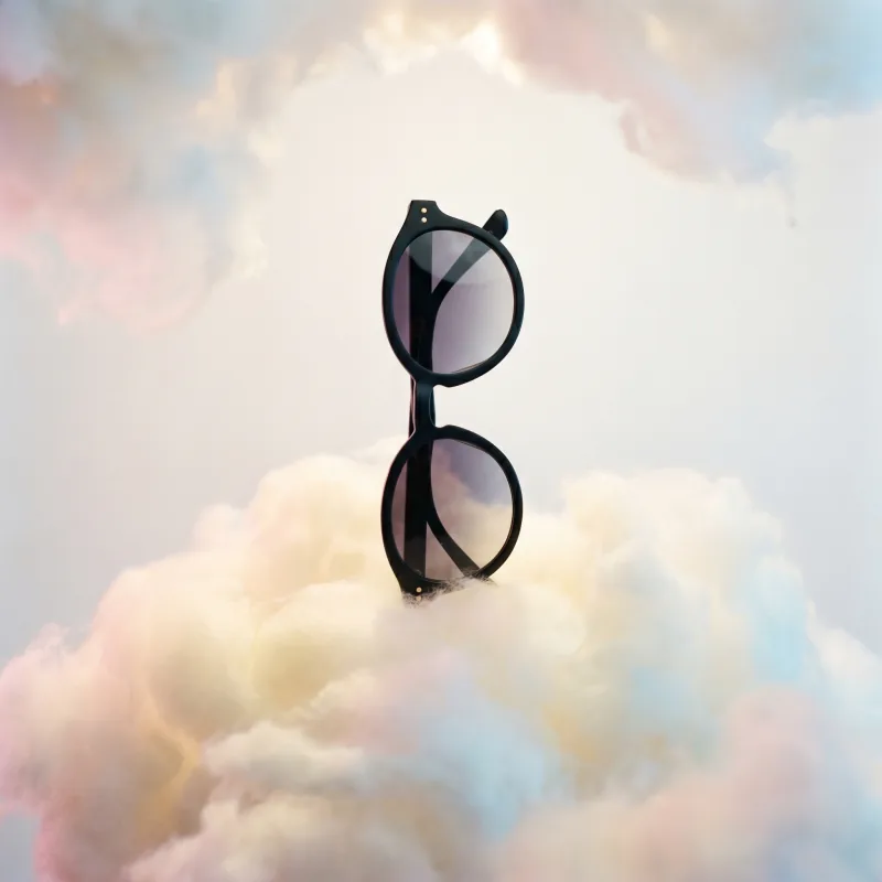 Whimsical theatrical editorial still-life of the same matte black sunglasses standing upright on a painterly buttery-cream and pale-blush pastel cloud, dreamlike soft daylight, Playcut generation