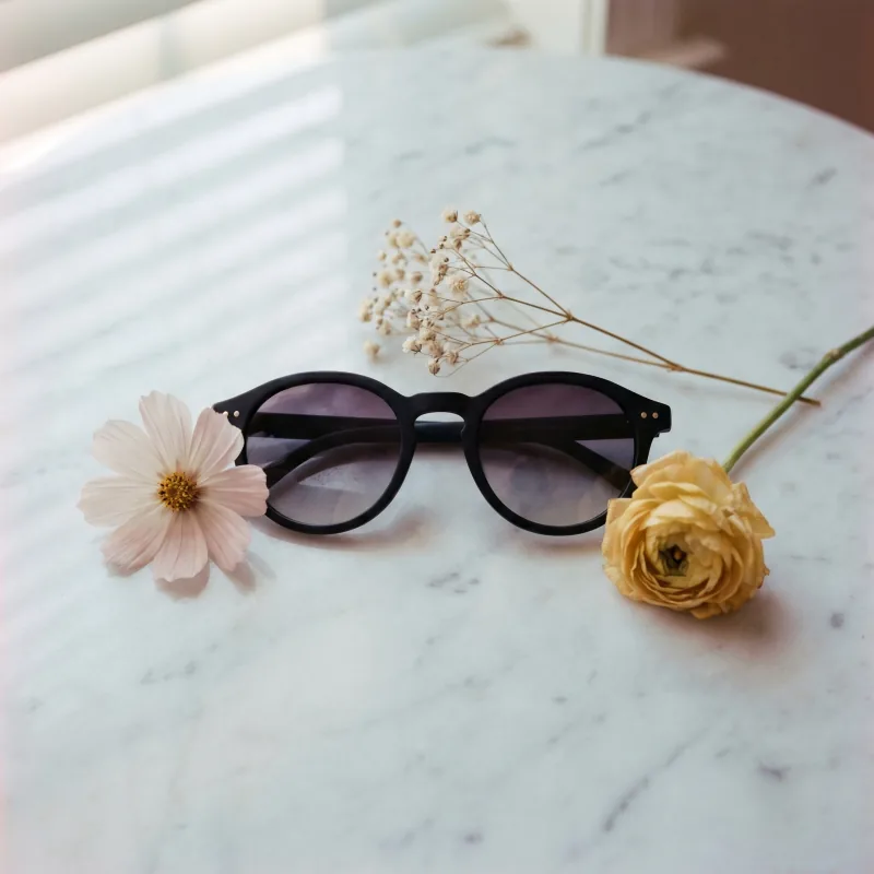 Editorial nature still-life of the same matte black sunglasses on Carrara marble surrounded by a cosmos flower, dried baby's breath and a butter-yellow ranunculus, slatted-blind shadow patterns, Playcut generation